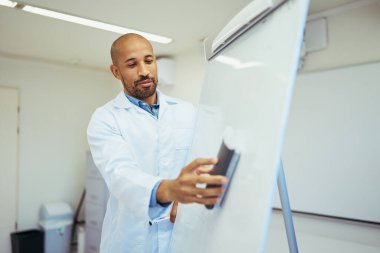 Parlak, modern bir hastanede beyaz tahtayı temizlemeye odaklanmış bir doktor, hijyen ve hazırlığın önemini vurguladı