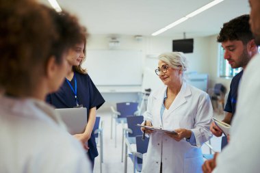 Doktorlar ve hemşireler, modern bir hastane konferans odasında yapılan bir toplantıda uzmanlıklarını paylaşıyor ve hasta vakalarını tartışıyorlar.