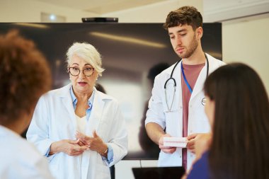 Doktorlar ve hemşireler, modern bir hastane ortamında profesyonel bir sağlık toplantısı sırasında uzmanlıklarını paylaşıyor ve tıbbi verileri analiz ediyorlar.