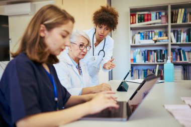 Doktorlar ve hemşireler hastanede birlikte çalışıyorlar, hasta bakımı ve tedavi stratejilerini tartışmak için dizüstü bilgisayar ve dijital tablet kullanıyorlar.