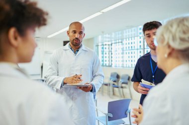 Doktorlar ve hemşireler, parlak ve modern bir hastane ortamında verimli bir toplantıda uzmanlıklarını paylaşıyor ve hasta bakımını koordine ediyorlar.