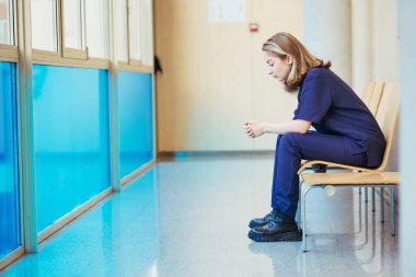 Genç hemşire ara veriyor ve modern bir hastane koridoruna yansıyor. Düşünme ve dinlenme hissi veriyor.