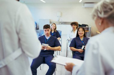 Tıp konferansı sırasında konuşmacı dinleyen doktorlar ve hemşireler, takım çalışmasını vurgulayarak ve sağlık hizmetlerinde devam eden eğitimi