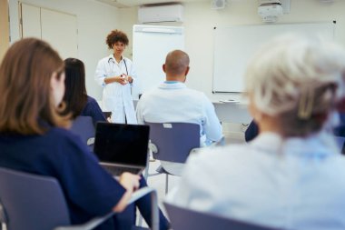 Modern bir hastane ortamında takım çalışmasını ve işbirliğini teşvik eden, sağlık uzmanları için bir eğitim oturumuna başkanlık eden kadın doktor
