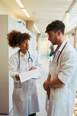 İki doktor hastane koridorunda tıbbi bir raporu inceliyor ve bir hasta vakasını tartışıyorlar.