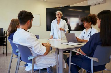 Tıp brifingine katılan doktorlar ve hemşireler, çağdaş bir hastane ortamında hasta bakımı stratejileri üzerinde işbirliği yapıyorlar.