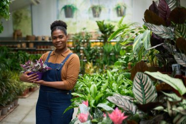 Canlı bir fabrikada çalışan genç bir kadın elinde bir tradescantia zebrina tutarken gülümsüyor ve bahçe işlerine olan tutkusunun tadını çıkarıyor.