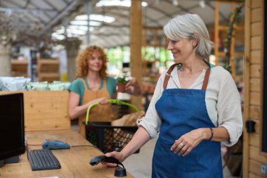 Dost canlısı, olgun bir kasiyer, bir bahçe merkezindeki kasada mükemmel müşteri hizmetleri sunuyor.