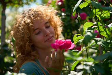 Genç bahçıvan yaz güneşinde pembe bir gülün kokusunun tadını çıkarıyor. Etrafı yemyeşil bir gül bahçesiyle çevrili.