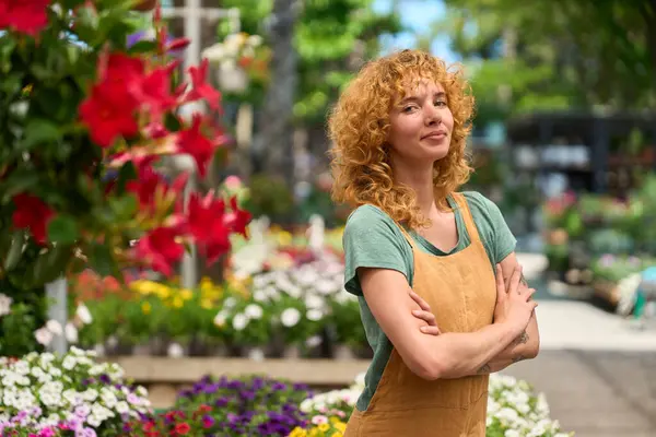 Çapraz kollarla poz veren gururlu çiçekçi, canlı, renkli bir çiçekçide uzmanlığını ve tutkusunu sergiliyor.