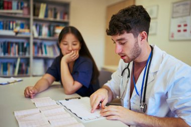 Hastane kütüphanesinde hasta çizelgeleri üzerinde işbirliği yapan tıp uzmanları, sağlık hizmetlerinde takım çalışması ve uzmanlık gösteriyorlar.