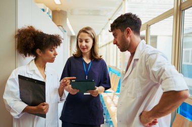 Doktorlar ve hemşire dijital tabletin tıbbi kayıtlarını inceliyor, modern sağlık hizmetlerinde işbirliği ve teknolojinin altını çiziyor