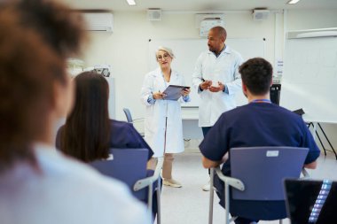 Parlak bir hastane sınıfında tıp konferansına katılan doktorlar ve hemşireler teşhis ve tedavi stratejilerini tartışıyorlar.