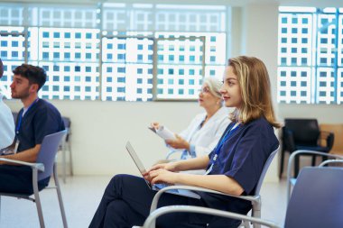 Doktorlar ve hemşireler dizüstü bilgisayar kullanıyorlar, notlar alıyorlar ve parlak bir hastane ortamında tıbbi konferansa katılıyorlar.