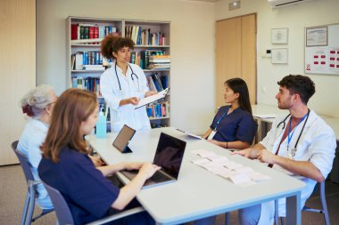 Doktorlar ve hemşireler tıbbi brifinge katılıyor, modern bir hastane ortamında hasta bakımı ve tedavi stratejileri üzerinde işbirliği yapıyorlar.