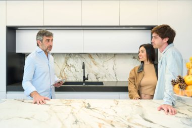 Modern mobilya galerisindeki bir çifte çeşitli mutfak tasarım seçenekleri sunan iç mimar, stil ve materyalleri tartışıyor.