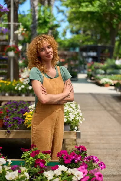 Genç bir kadının portresi bir bitkide çalışıyor, renkli çiçeklerin arasında çapraz kollarla rahatça poz veriyor.