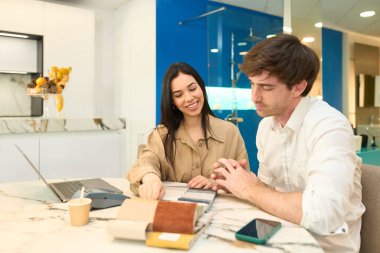 Modern bir mobilya galerisinde iç mimarın yardımıyla malzeme ve kumaş seçen genç bir çift.