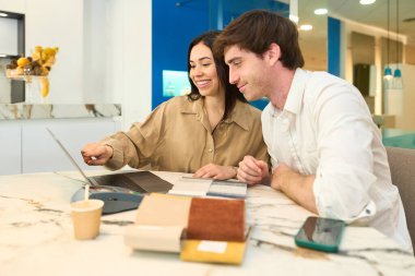 Yeni daireleri için mobilya ve döşemeyi seçen çift modern bir mobilya galerisinde danışmanıyla birlikte dizüstü bilgisayar kullanıyor.
