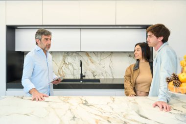 Modern mobilya galerisindeki bir çifte çeşitli mutfak tasarım seçenekleri sunan iç mimar, stil ve materyalleri tartışıyor.