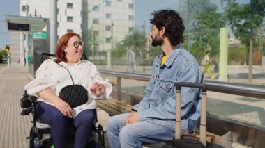 Tekerlekli sandalyedeki engelli bir kadınla otobüs durağındaki bavullu genç bir gezgin arasında neşeli bir sohbet.