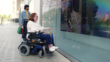 Bir kadın arkadaşıyla birlikte motorlu sandalye vitrinlerini kullanıyor, kentsel yaşam tarzının tadını çıkarıyor ve perakende satış mağazasının yakınındaki bağlantı anını paylaşıyor.