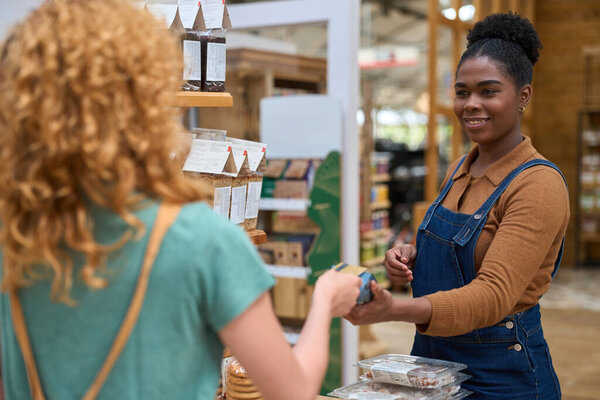 Friendly employee scanning groceries for a customer making a contactless payment at a sustainable grocery store