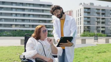 Kapsamlı sağlık rehberliği için tablet kullanan profesyonel sağlık hizmeti sağlayıcısı, dış danışma sırasında engelli hastalarla tıbbi detayları paylaşıyor