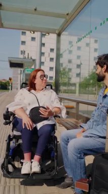 Keyifli engelli kadın otobüs durağında beklerken arkadaşlarıyla dostça sohbet ediyor, hareket kabiliyeti, sosyal bağlar ve kapsayıcı yaşam tarzı gösteriyor.