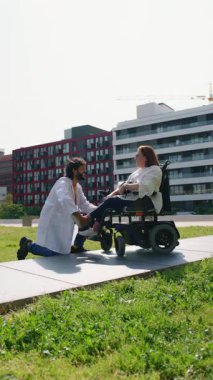 Hastane ortamında tekerlekli sandalyede oturan kadın hastaların ayaklarını dikkatlice muayene eden profesyonel bir doktor.
