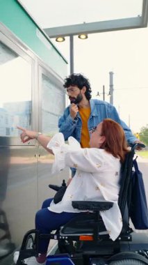 Otobüs durağındaki otobüs tarifesine bakarak tekerlekli sandalyedeki bir kadına yardım eden yardımsever bir adam.