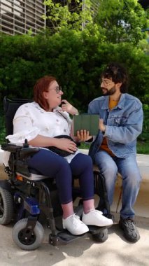 Tekerlekli sandalye kullanan neşeli bir kadın, bir erkek arkadaşıyla dijital tablet kullanmaktan zevk alır.