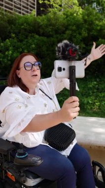 Şehir parkında gezinen güçlendirilmiş içerik yaratıcısı, akıllı telefon ve mikrofon kullanarak sosyal medya videolarını kaydediyor.