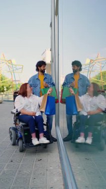 Tekerlekli sandalyedeki neşeli kadın alışveriş torbaları sergiliyor, şehir gezisinde arkadaşlarıyla heyecanı paylaşıyor, çeşitliliği ve sosyal bağlantıyı temsil ediyor.