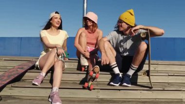 Neşeli genç patenciler, güneşli bir günün tadını çıkarıyorlar, birlikte gülüyorlar ve ahşap merdivenlerde oturuyorlar.