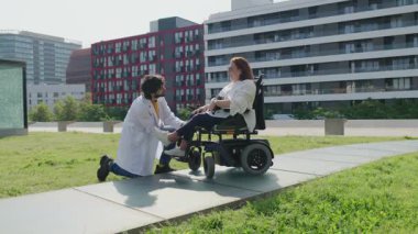 Tekerlekli sandalyedeki hastaya yardım eden bir tıp uzmanı, şehir parkındaki ayak takımını düzeltiyor.