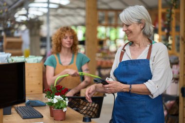 Neşeli, olgun bir kasiyer. Parlak bir bitki bakım odasındaki kasada çiçek tarıyor. Mükemmel müşteri hizmetleri sunuyor.