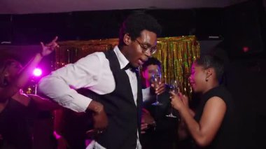 Dostlar neşeyle dans ediyor, şenlikli yeni yıl arifesinde şampanya kadehleri tokuşturuyor altın ışıklar ve enerjik ruh haliyle ışıl ışıl gece klübünde kutlama yapıyorlar.