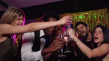 Mutlu çoklu etnik arkadaşlar kadehlerini şampanya kadehleriyle kaldırıyor yeni yıl partisinde, bir gece kulübünde, ağır çekimde.