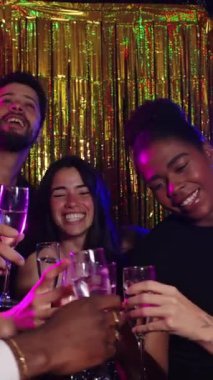 Yeni yıl arifesini kutlayan bir grup arkadaş, altın folyo perdesinin önünde şampanya kadehleriyle kadeh kaldırıyorlar.