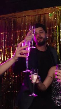 Neşeli bir grup genç arkadaş şampanyaya kadeh kaldırıyor, canlı yeni yıl arifesinde şenlikli gece kulübü atmosferinin tadını çıkarıyorlar. Parlak altın bir havayla kutlama yapıyorlar.