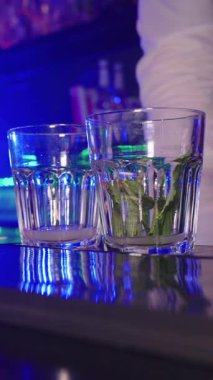Profesyonel barmen imzalı kokteyl, nane yapraklarını mavi gece kulübünün ışıkları altında ezilmiş buzla karıştırmak gösterişli bar tezgahında.