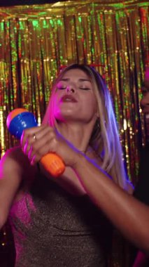 Arkadaşlar karaoke gecesinde enerjik bir düet yapıyorlar, altın arka plana karşı neşeli dinamik ifade ile neşeli bir şarkı anı paylaşıyorlar.