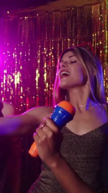 Arkadaşlar bir gece kulübünde tutkulu bir şekilde karaoke söylüyor, canlı mor ışıklarla aydınlatılıyor, canlı ve eğlenceli bir atmosfer yaratıyor.