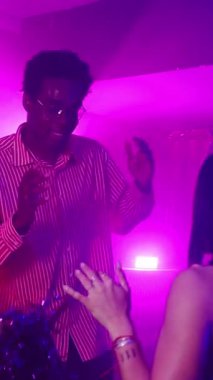 Gece kulübünde mor ışıkların altında yavaş çekimde dans eden gençler gece hayatı ve müziğin tadını çıkarıyorlar.