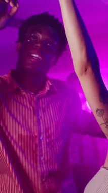 Enerjik arkadaşlar gece hayatından zevk alıyorlar, ritmik hareket ediyorlar ve bir gece kulübünde renkli ışıklar altında gülümsüyorlar.