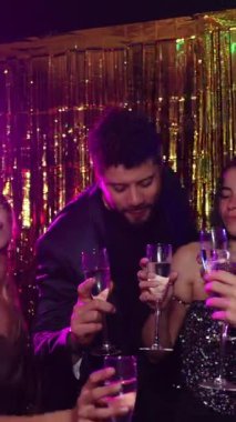 Bir grup zarif arkadaş yeni yıl arifesinde kadehlerini şampanya kadehleriyle kaldırırken altın arka planda, ağır çekim