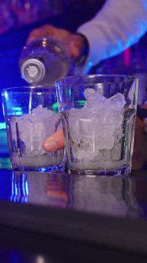 Profesyonel barmen alkollü içeceği gece kulübünde buzla dolu iki bardağa dolduruyor.