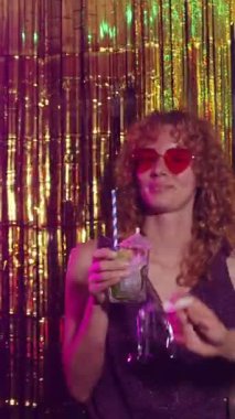 Pembe güneş gözlüklü genç kızıl kadın kokteyl içiyor ve baloncuklar üflüyor.