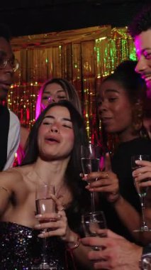 Neşeli çoklu etnik arkadaşlar kutlama yapıyor, fotoğraf kabini özçekimi için poz veriyorlar, yavaş çekimde şampanya kadehleriyle kadeh kaldırıyorlar.